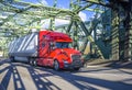 Long haul bright red big rig semi truck transporting cargo in dry van semi trailer running on the arched truss bridge