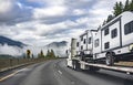 Long haul high cab white big rig semi truck transporting campers trucks on the step down semi trailer driving on the winding Royalty Free Stock Photo