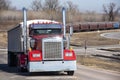 Long haul 18 wheeler semi truck hauling freight driving on road with diesel train and boxcars in background.