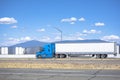 Long hauler blue big rig semi truck transporting cargo in dry van semi trailer drives past a truck stop on California plateau