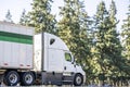 Long hauler high cab big rig white semi truck transporting cargo in dry van semi trailer driving on the highway road with trees on Royalty Free Stock Photo