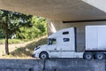 Long hauler white big rig bonnet semi truck transporting cargo in dry van semi trailer driving on the divided highway road under Royalty Free Stock Photo