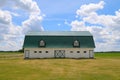 A long horizon view of a bright white farm barn with green trim and green tin rood in a grass field Royalty Free Stock Photo