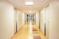 Long hospital corridor with light walls colorful floor and ceiling with plafone lamps illuminated. Health care and medical backgr