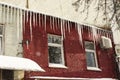 Long icicles hang from the snow-covered roof of an old red brick building. Winter, Christmas city landscape, background Royalty Free Stock Photo