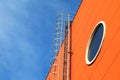 A long iron staircase on the orange wall of a modern industrial building with a round window against a blue sky Royalty Free Stock Photo
