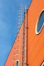 A long iron staircase on a orange wall of a modern industrial building with a round windows against a blue sky Royalty Free Stock Photo