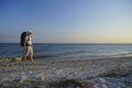 A guy with a backpack walks along the coastline in the evening barefoot on the sand, holds sandals in his hand Royalty Free Stock Photo