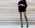 A long-legged girl in fashionable pantyhose, a black dress and black high-heeled shoes posing in the summer on wooden steps. Fashi Royalty Free Stock Photo