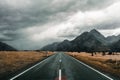 long lonely road crossing a quiet field with few trees and sparse vegetation leading to mountains under a sky with lots Royalty Free Stock Photo