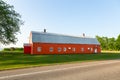 Long metal-clad orange barn with grey roof seen close to the road during a beautiful sunny spring morning