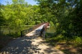 A long metal rust colored bridge over a lake surrounded by lush green trees and plants with blue sky at Cauble Park Royalty Free Stock Photo