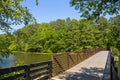 A long metal rust colored bridge over a lake surrounded by lush green trees and plants with blue sky at Cauble Park Royalty Free Stock Photo