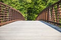 A long metal rust colored bridge over a lake surrounded by lush green trees and plants with blue sky at Cauble Park Royalty Free Stock Photo