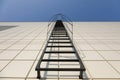 Long metal staircase on the gray modern facade of an industrial building, warehouse or shopping center against the blue Royalty Free Stock Photo