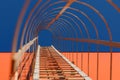 Long metal staircase on an orange modern facade of an industrial building, warehouse or shopping center against the blue sky. Royalty Free Stock Photo