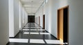 Long modern white hallway with repeating doors and sunlight casting geometric shadows on the floor corridor Royalty Free Stock Photo