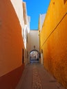 Long narrow alley in ciutadella town menorca with a bright yellow wall and archway at the end with a blue summer sky
