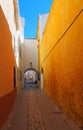 Long narrow alley in ciutadella town menorca with a bright yellow wall and archway at the end with a blue summer sky