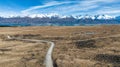 Long narrow gravel road across rural agricultural countryside towards the snow capped Southern alps mountain range Royalty Free Stock Photo