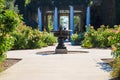 A long paved footpath with a fountain in the center with lush green trees along the path a pink and yellow roses