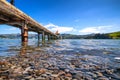 A long pier at Akaroa, New Zealand. The water is so clear that one can see pebbles under the water. There are rolling hills in the Royalty Free Stock Photo