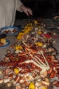 Long pile of seafood including crab legs shrimp and crayfish with sausage corn and potatoes down long table with person using