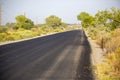 Long plain asphalt road lined by fencing and power poles