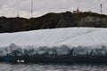 Long Point Lighthouse at the top of cliff in Twillingate Harbour with large iceberg in foreground Royalty Free Stock Photo