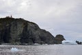 Long Point Lighthouse at the top of cliff in Twillingate Harbour with large iceberg stranded nearby Royalty Free Stock Photo