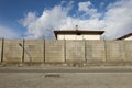Long precast concrete wall with barbed wire on top. Sidewalk and street in front, blue cloudy sky above. Background for copy space
