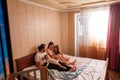 Long range shot of beautiful family on the bed in the morning in the sun from window. General view