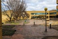 A long red brick footpath surrounded by bare winter trees, tall circular light posts, lush green plants, bike racks