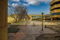 A long red brick footpath surrounded by bare winter trees, tall circular light posts, lush green plants, bike racks