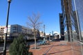 A long red brick sidewalk next to a marble building with electric bikes, bare winter trees, lush green plants