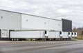 Long refrigerator semi trailers stand in row in warehouse docks with gates and loading cargo