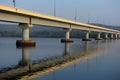 Long road bridge over the river, side view. Powerful stone columns of bridge are reflected in the river water against the shore Royalty Free Stock Photo