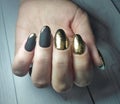 Long round nails with black matte gel polish and gold design. Manicure on women`s hands with gel coating. Royalty Free Stock Photo