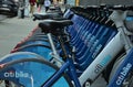 Long row of Citibike corporate sponsored bike share bicycles docked in a dock bay on a street in New York City.