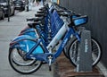 Long row of Citibike corporate sponsored bike share bicycles docked in a dock bay on a street in New York City.