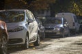 Long row of different cars and vans parked along roadside on sunny autumn day on blurred green golden foliage bokeh background. Royalty Free Stock Photo