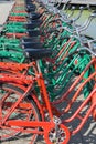 Long row of green and red bicycles with black seats and cargo racks in back for hire in urban street
