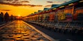 Long row of metal shopping carts standing near the shop at sunset. People walk by the paved road beside. Low angle view. Royalty Free Stock Photo