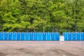 Long row of portable toilets in front of a forest where one has tipped over Royalty Free Stock Photo