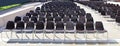 Long rows of empty black plastic chairs geometrically arranged under the sun. Royalty Free Stock Photo