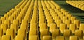 Long rows of empty yellow plastic chairs geometrically arranged on a lawn.