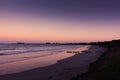 Long sandy beach at sunset with purple skies and water