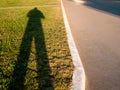 Long Shadow Of A Man Casting On Green Lawn At Sunset. Curved Curb And Sidewalk.