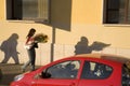 Long shadows of woman carrying flowers near red car in Rome Italy
