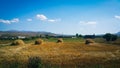 A long shot of hay bales gathered together on a wheat field on a hot and Sunny summer day, far visible houses, mountains and very